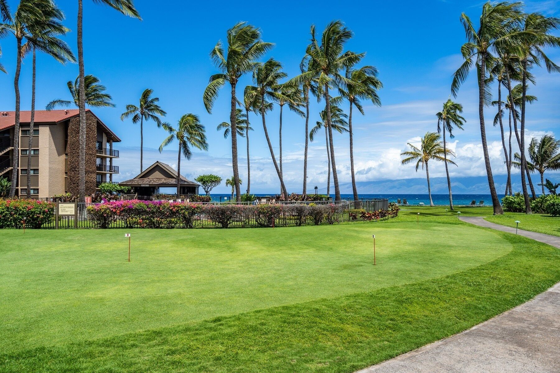 Un campo de golf con un club de campo, palmeras y vista al océano.