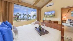 A hotel room with a large bed, a ceiling fan, a TV, and a view of palm trees and a beach. - Papakea H404 3 Bedroom Condo by RedAwning (Lahaina)