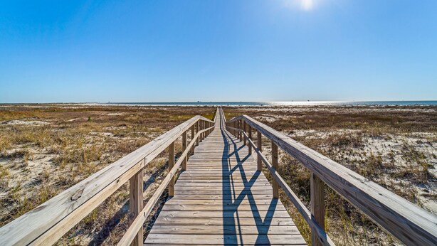 A wooden boardwalk leading to a beach with a clear sky and sun. - Dauphin Island Beach Club 310B Budget Friendly near the Beach!! (Dauphin Island)