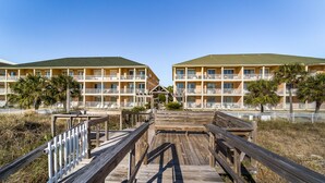 A wooden boardwalk leading to a hotel with multiple balconies and a green roof. - Dauphin Island Beach Club 310B Budget Friendly near the Beach!! (Dauphin Island)