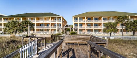 Un paseo marítimo de madera que conduce a un hotel con varios balcones y un techo verde.