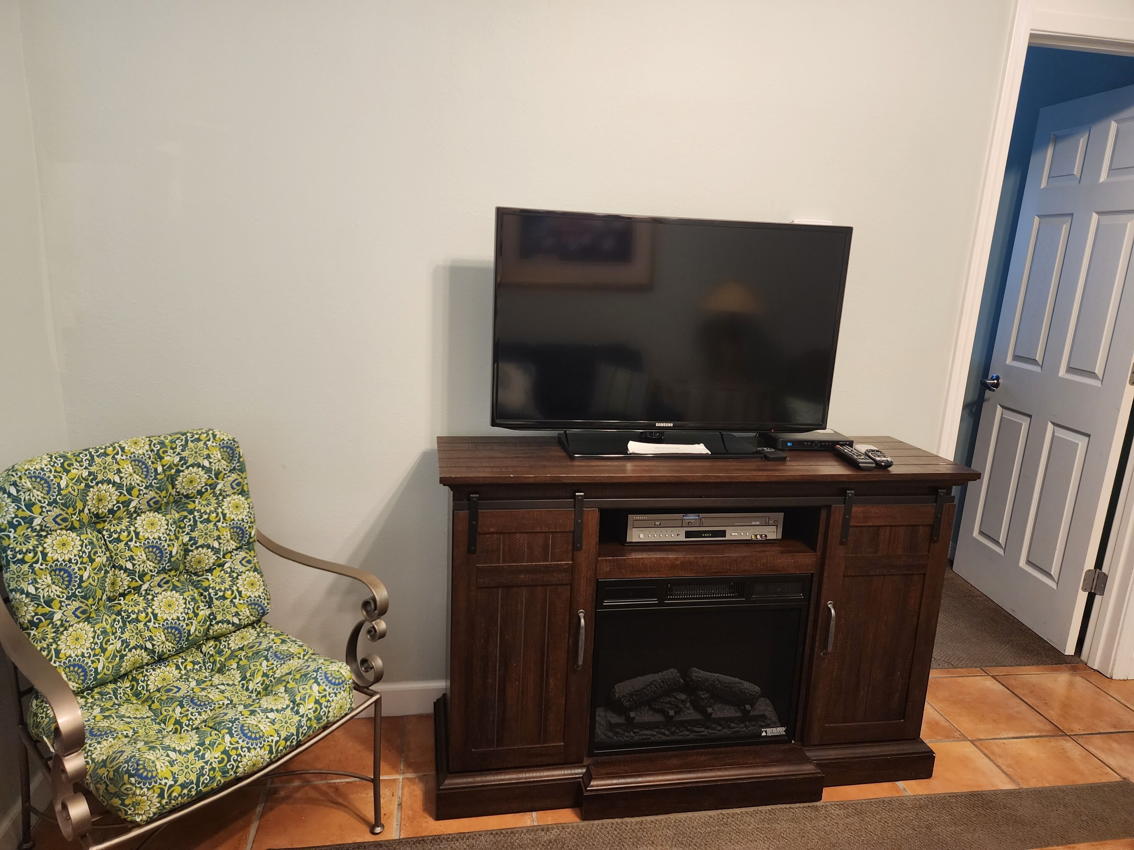 Un salon avec un téléviseur à écran plat posé sur un meuble en bois, un fauteuil à motifs et une cheminée située sous le téléviseur.