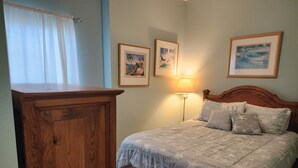 A bedroom with a wooden cabinet, a bed with patterned bedding, and three framed pictures on the wall. - Dauphin Island Beach Club 310B Budget Friendly near the Beach!! (Dauphin Island)