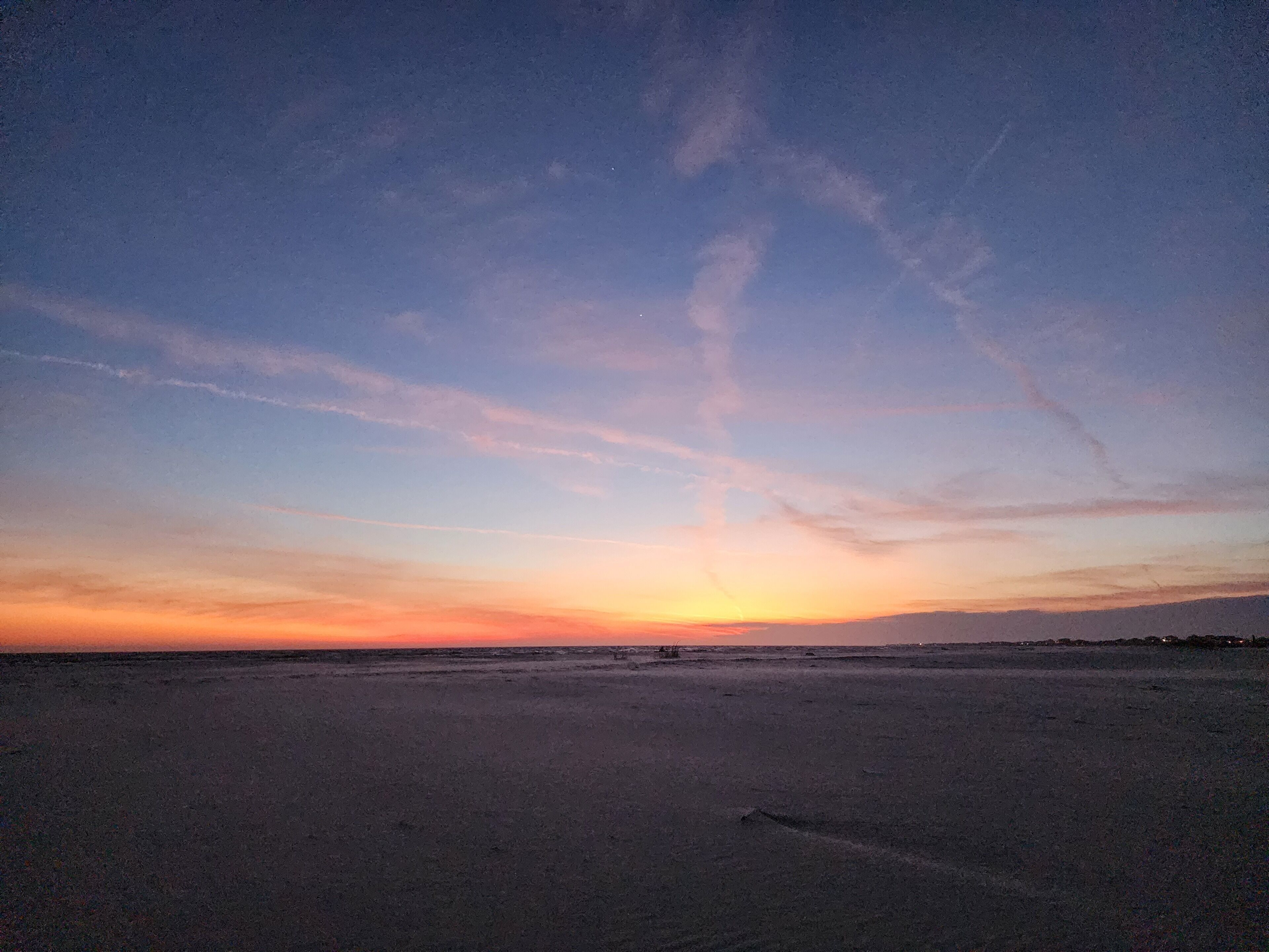 Ein Strand bei Sonnenuntergang mit klarem Himmel und weiter Ferne.