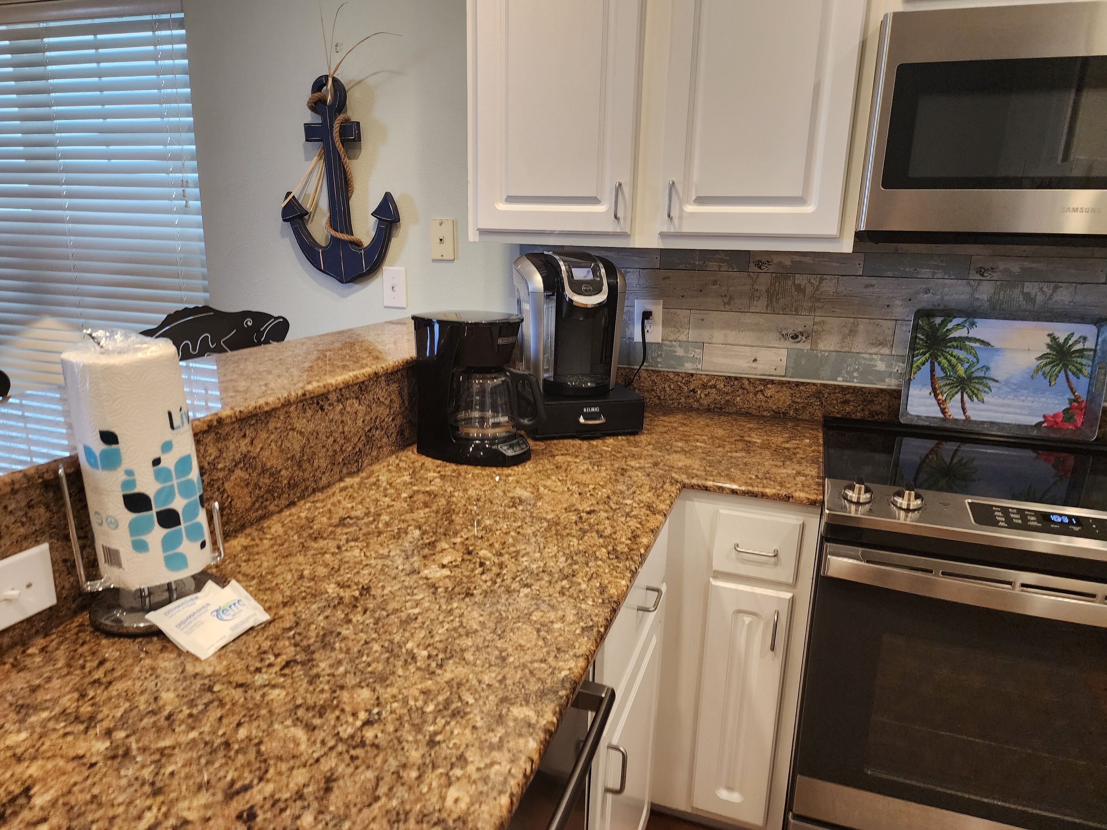 A kitchen with granite countertops, white cabinets, a coffee maker, a microwave, and an oven.