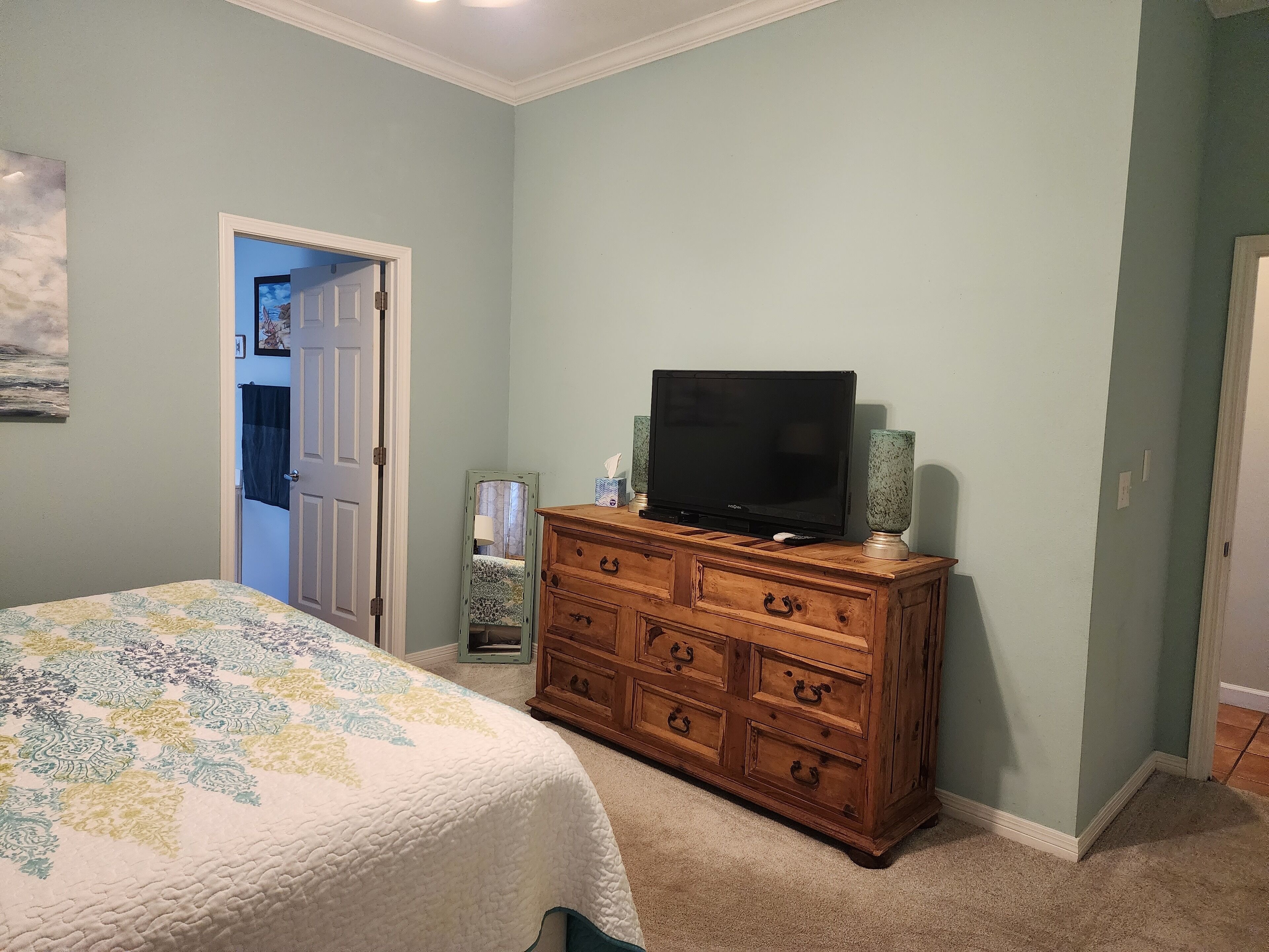 Un dormitorio con cama, cómoda de madera, televisor y puerta que da a otra habitación.