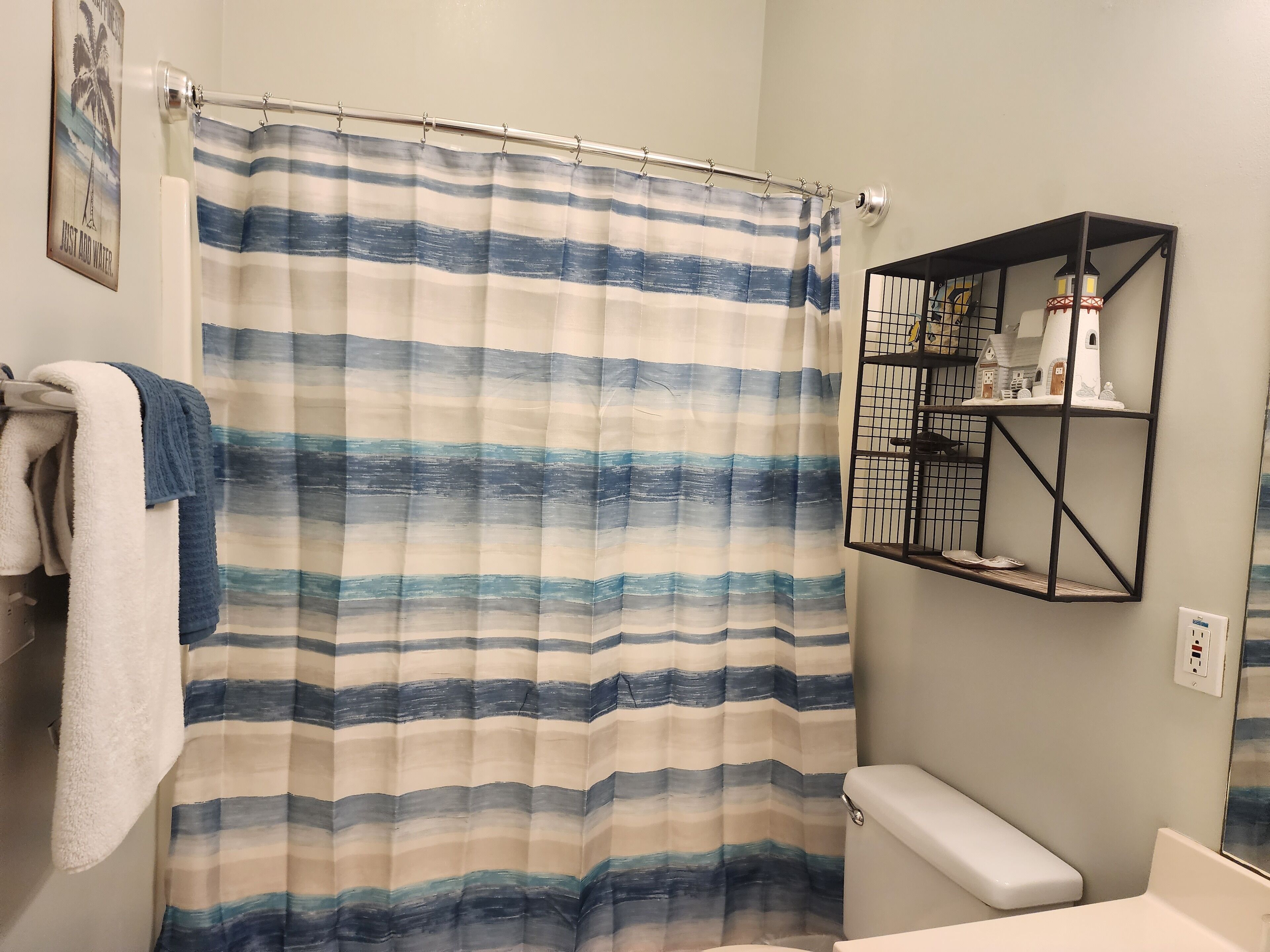 A bathroom with a striped shower curtain, a towel rack with a towel, a black metal shelf with decorative items, and a toilet.