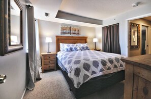 A hotel room with a bed, two bedside tables, a nightstand, a wooden dresser, a mirror, and a painting on the wall.