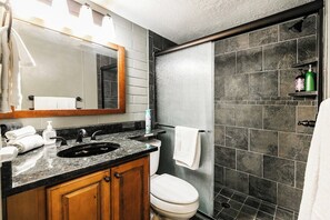A bathroom with a sink, mirror, toilet, and shower area.