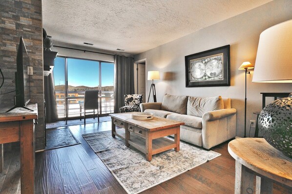 A modern living room with a sofa, coffee table, and a large window offering a view of the landscape.