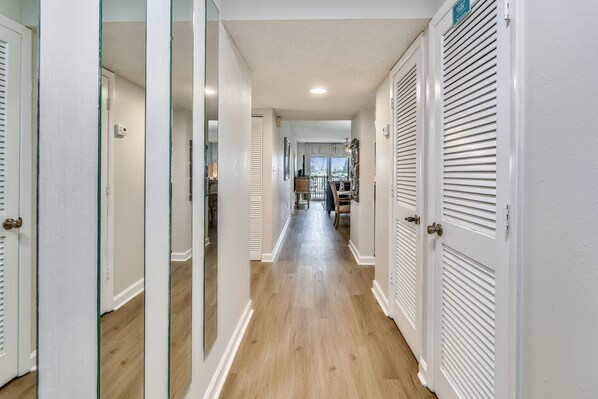 Un pasillo con puertas blancas, piso de madera y vista hacia un comedor.
