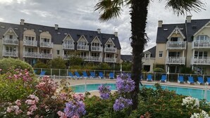 A hotel with multiple balconies, a swimming pool, and lush flower beds.