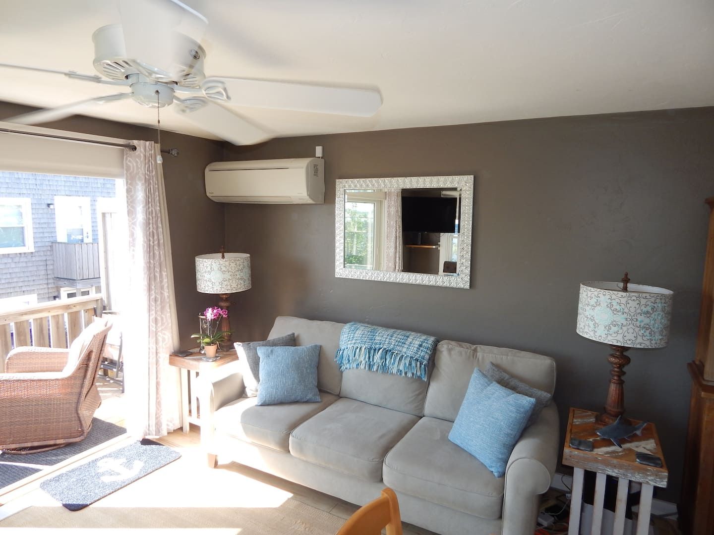 A living room with a sofa, two lamps, a ceiling fan, and a window.