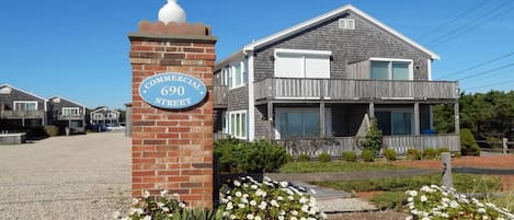 A two-story house with a balcony on the second floor, a brick pillar with a street sign, and a gravel driveway.