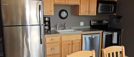 A modern kitchen with stainless steel appliances, wooden cabinets, a sink, and a dining area with two chairs.