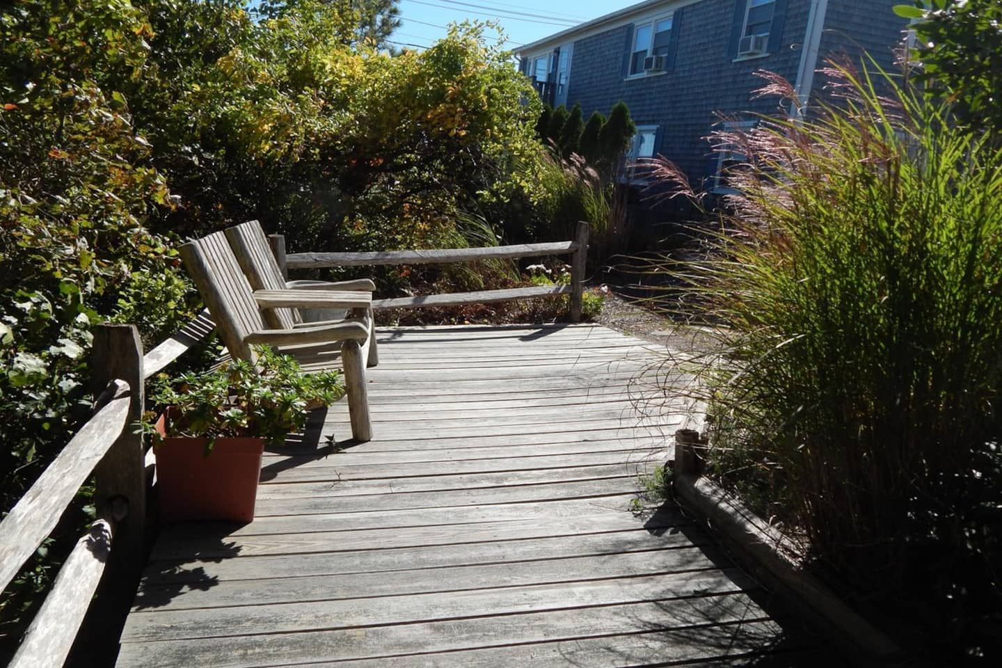 A wooden deck with a bench and potted plants, leading to a building.