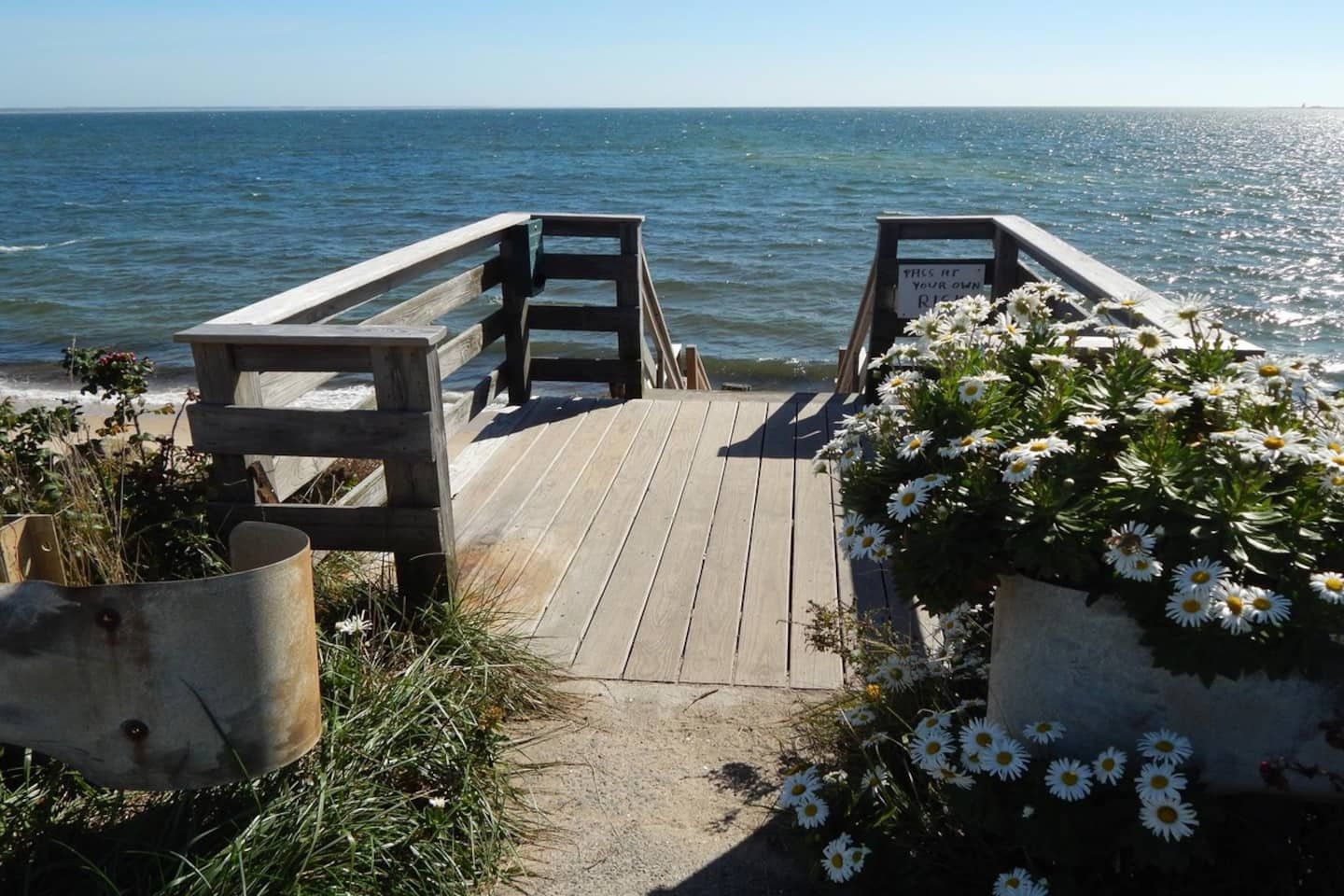 Un molo di legno che conduce a una spiaggia, con un cartello che recita 'THIS IS YOUR OWN RIDE'.