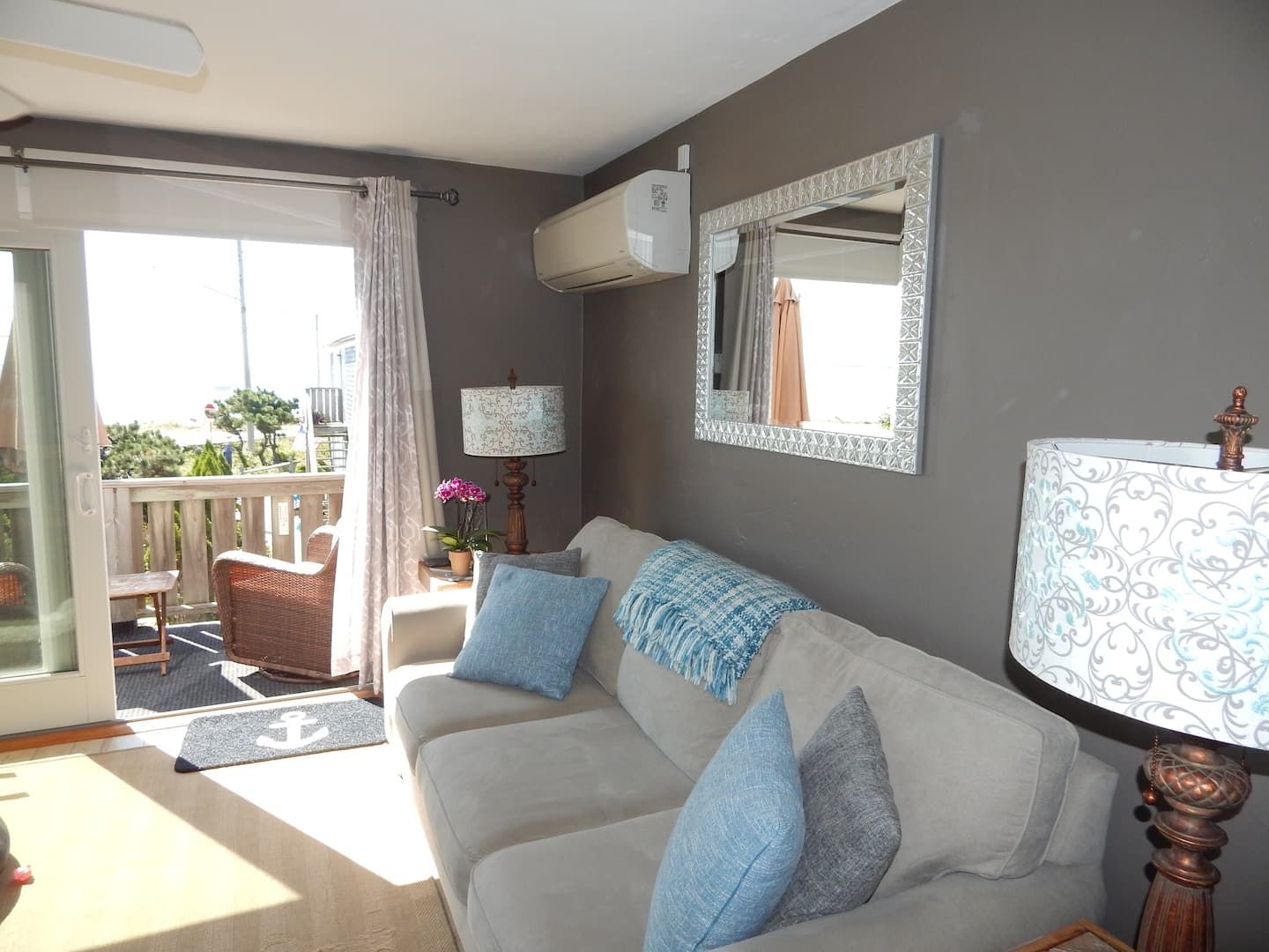 A living room with a sofa, a lamp, a mirror, and a sliding door leading to an outdoor area.