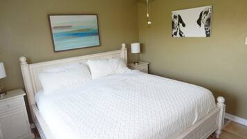 Quarto com cama, mesa de cabeceira, luminária, ventoinha no teto e duas obras de arte nas paredes.