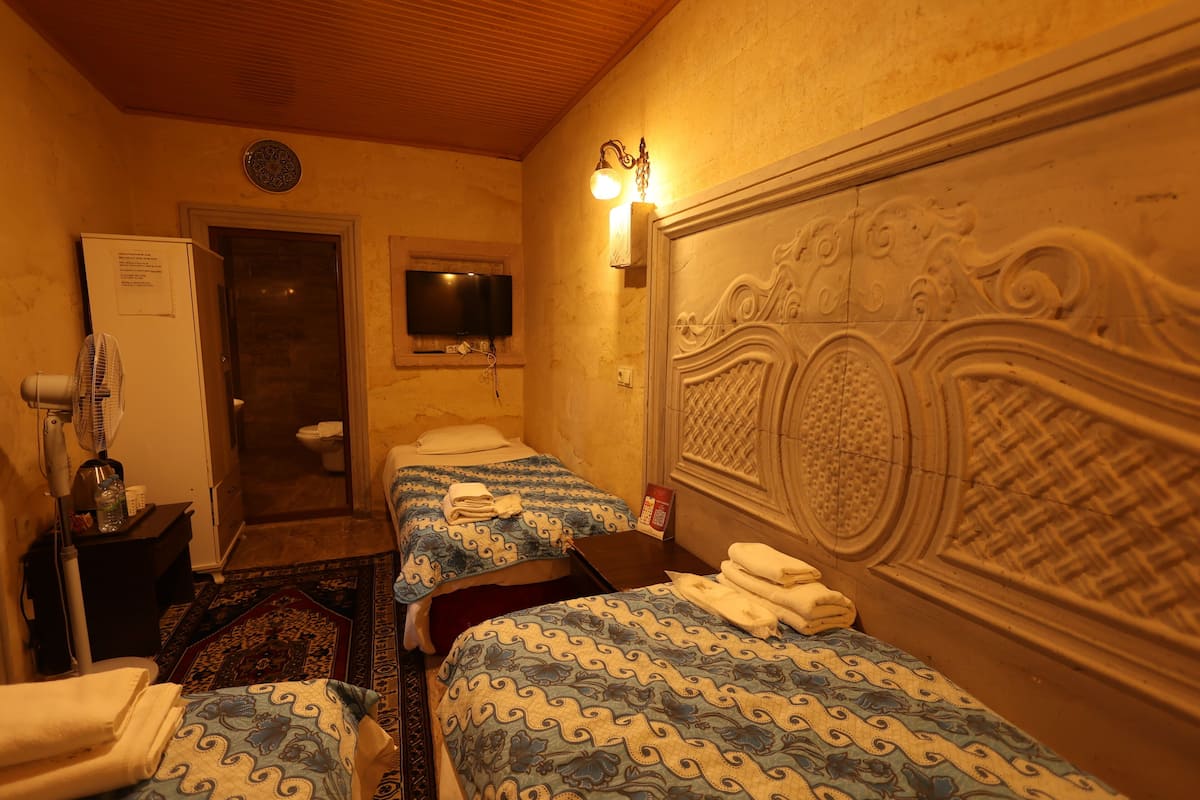 A hotel room with two beds, a television, a fan, and a door leading to a bathroom.