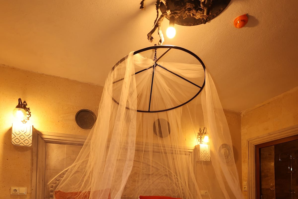 A bed with a canopy, white linens, red pillows, and a red throw blanket.
