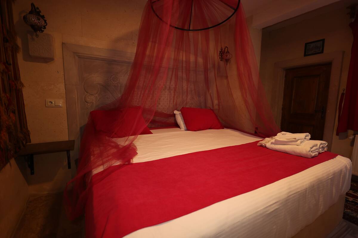 A bed with a red canopy, white bedding, and red pillows. There are folded white towels on the bed.