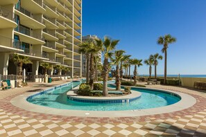 Un espace piscine d’hôtel offrant une vue dégagée sur l’océan, les palmiers et un immeuble à plusieurs étages doté de balcons.