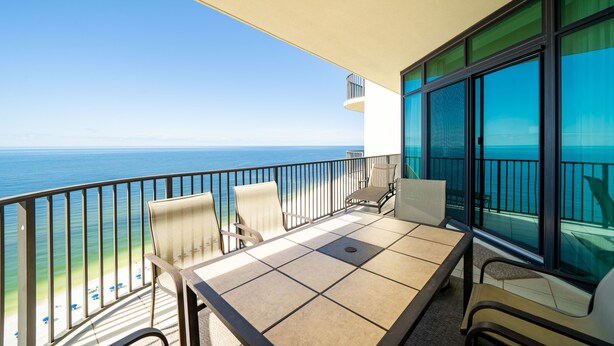 A balcony with a table and chairs, overlooking a beach and the ocean.