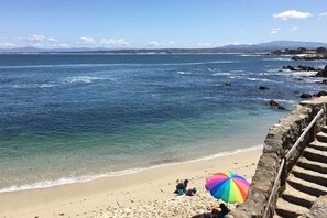 A beach with clear blue water, a sandy shore, and a colorful umbrella. - Daffodil House - Pacific Grove House - Block to the Beach (Pacific Grove)