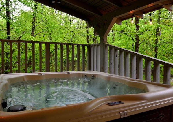 Un bain à remous installé sur une terrasse en bois, entouré d’une végétation luxuriante.