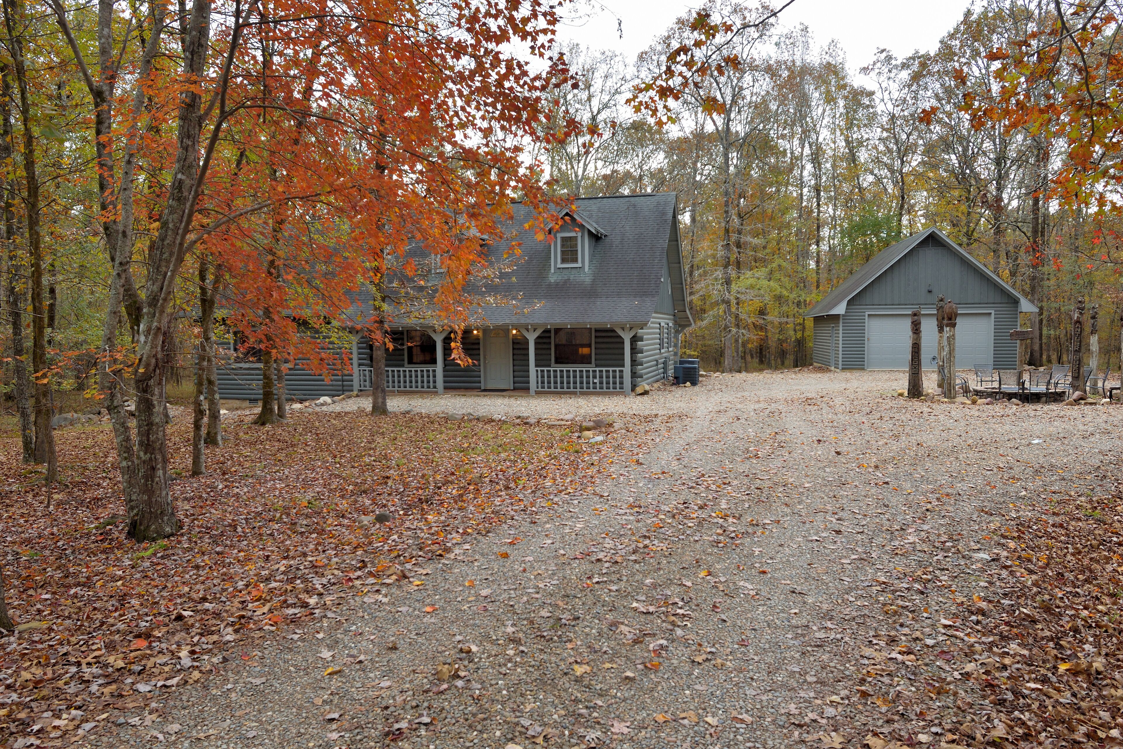 A rustic cabin with a porch and a garage, surrounded by trees with autumn leaves.