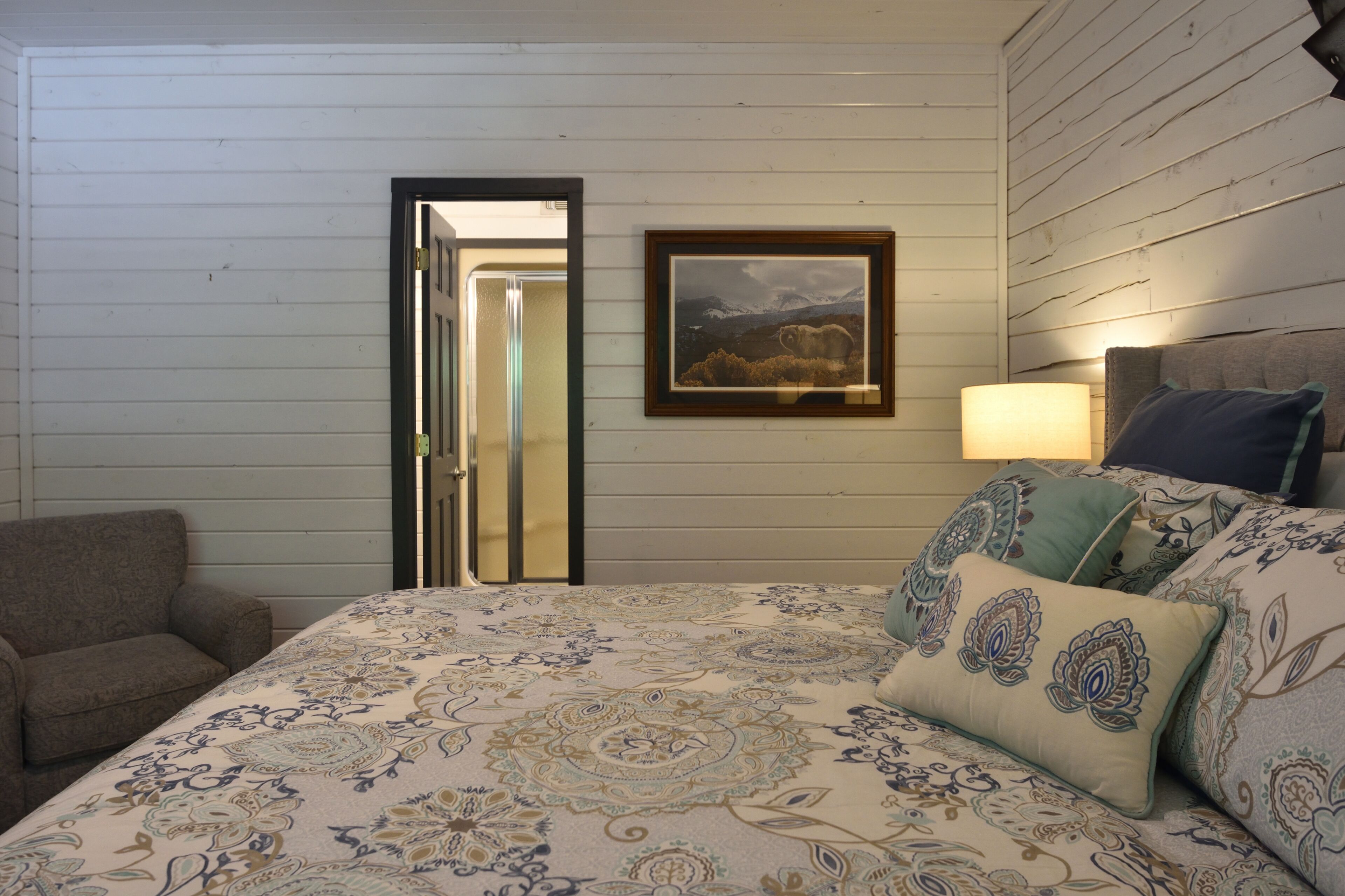A bedroom with a bed, a chair, a framed picture, and a door.