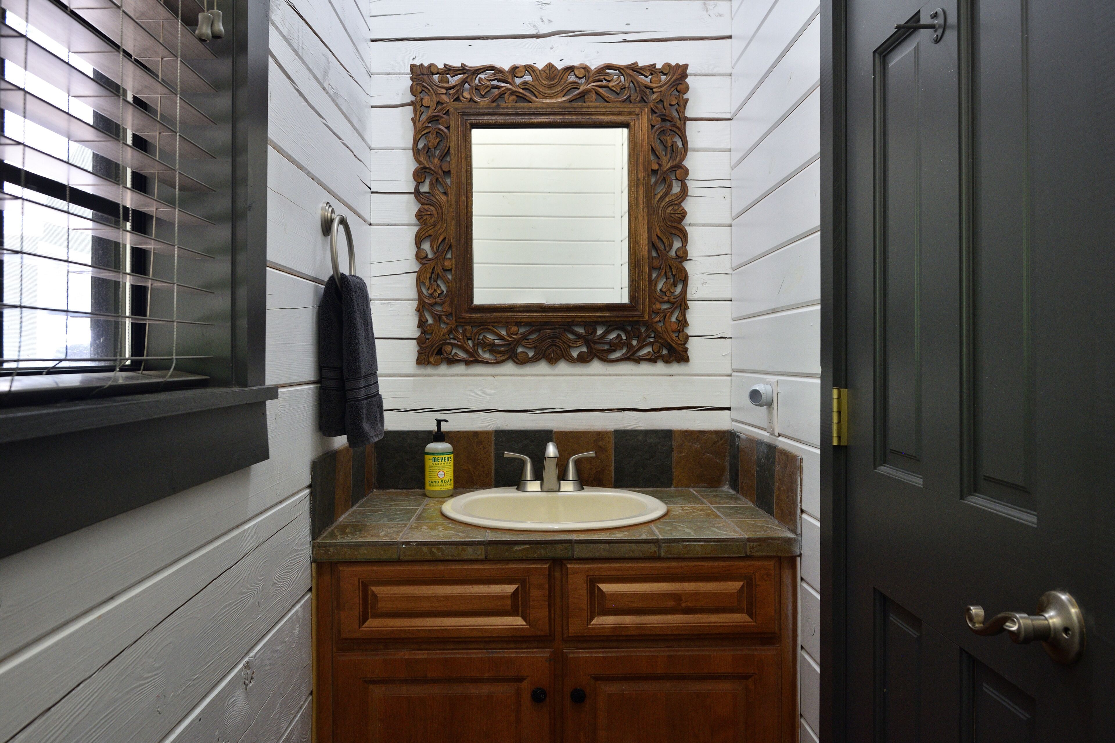 Un baño con tocador de madera, lavamanos y espejo con marco decorativo.