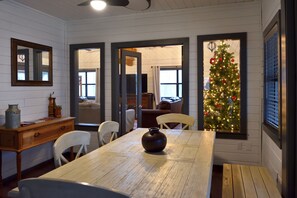Un coin repas avec une table en bois, des chaises et un vase. On peut apercevoir un sapin de Noël à travers une fenêtre.