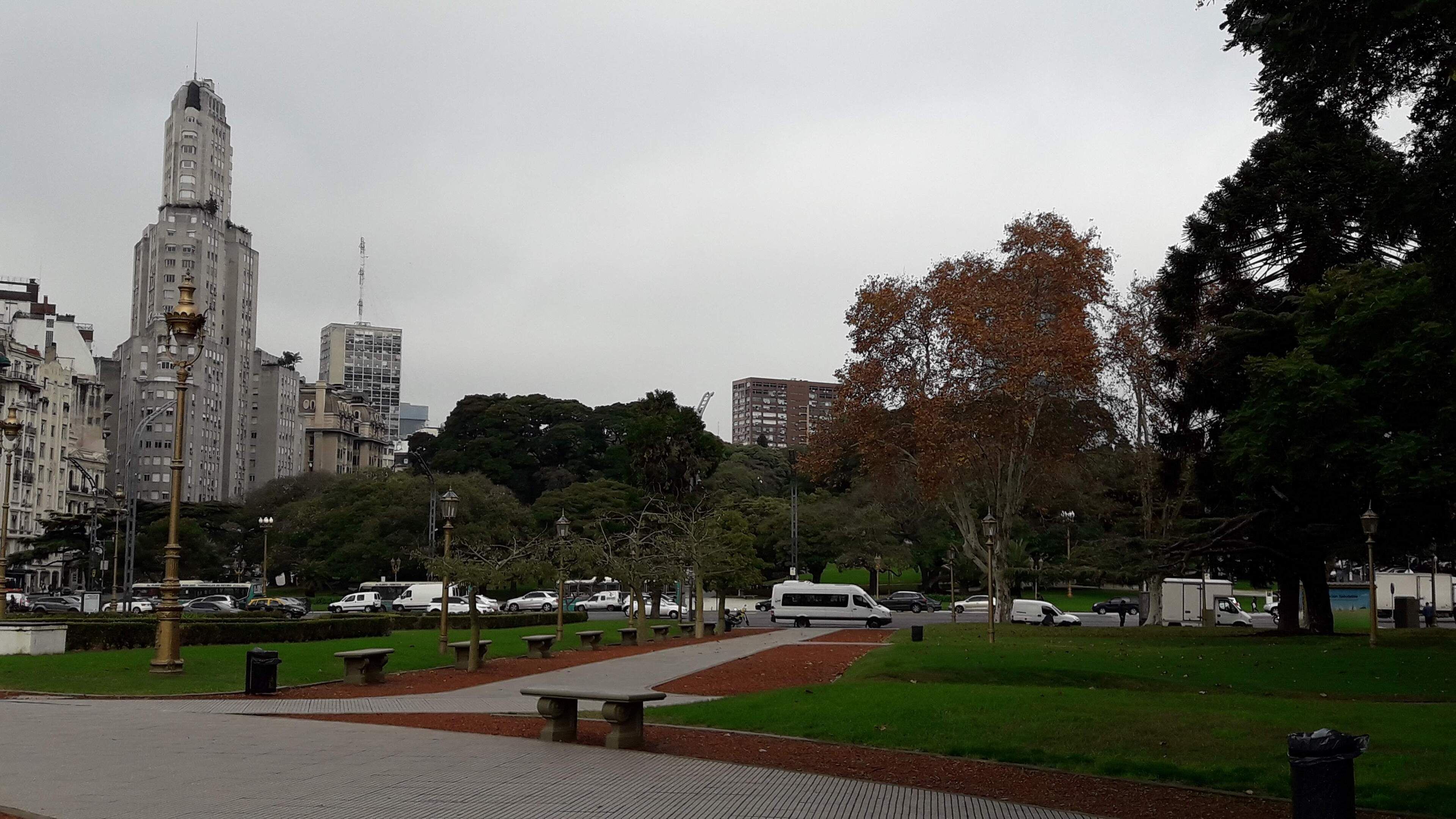 A park with a paved walkway, benches, and trees.