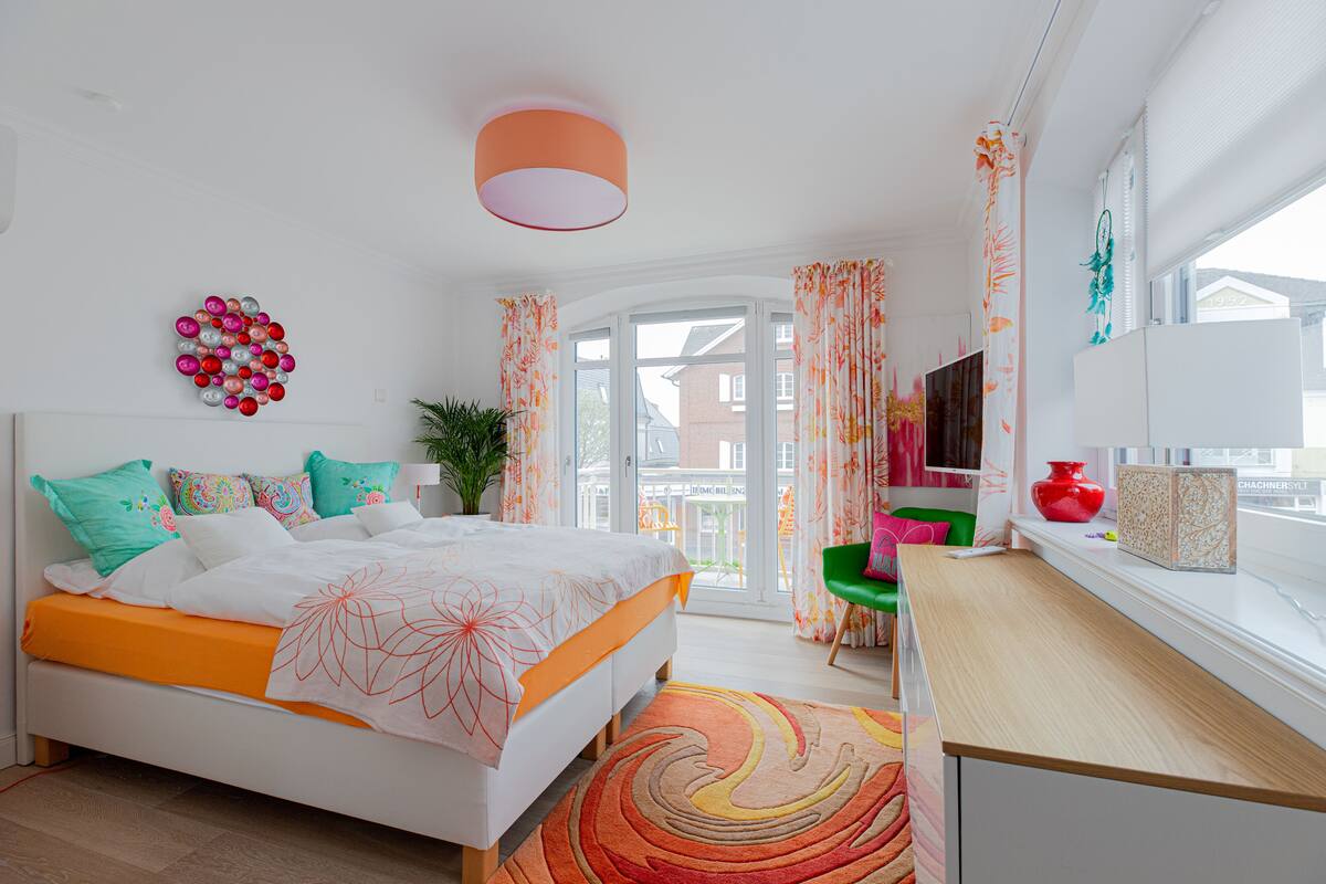 Een moderne slaapkamer met een bed, een bureau, een televisie en een raam met gordijnen.