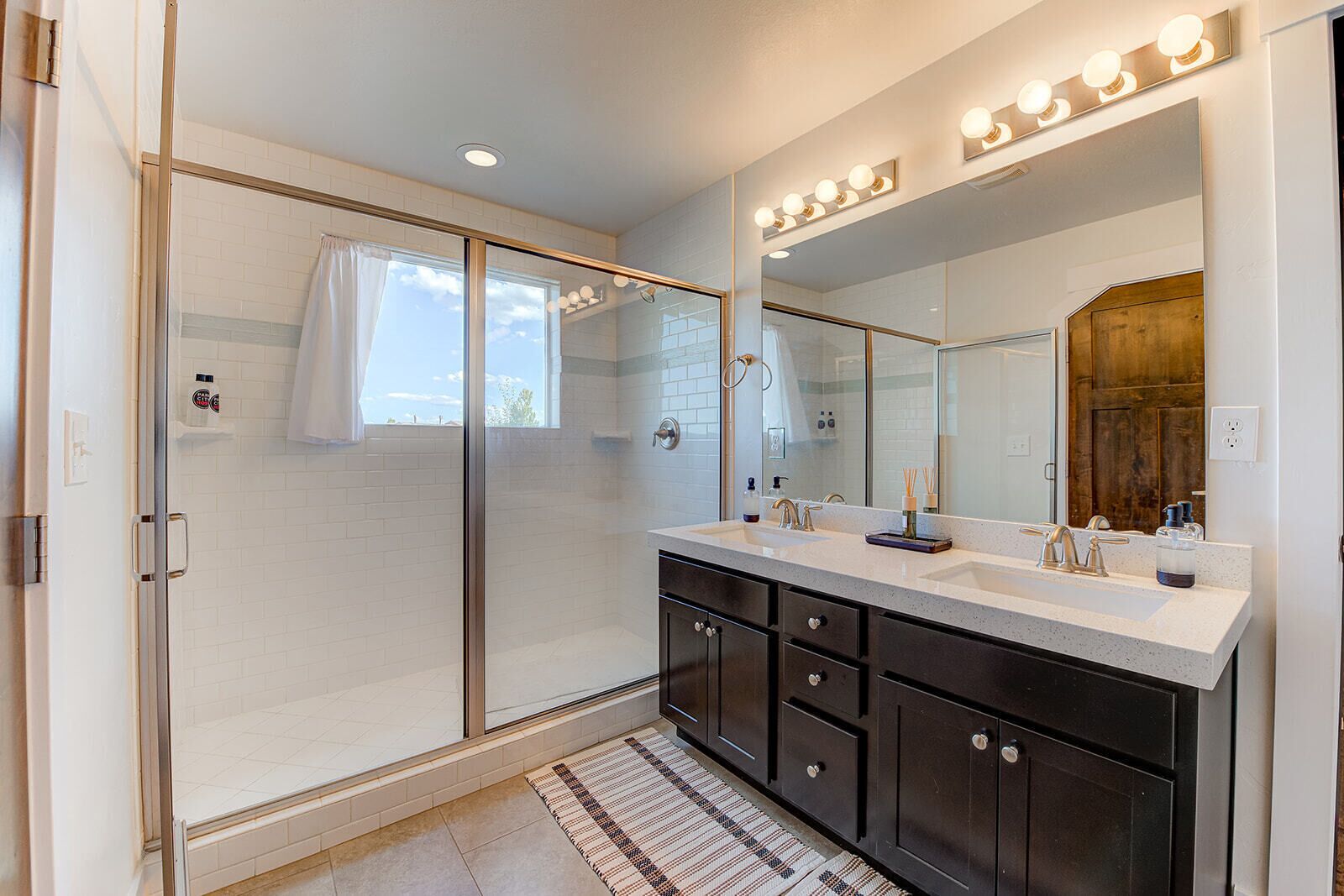 A modern bathroom with a glass shower enclosure, a vanity with a large mirror, and a lighted vanity area.