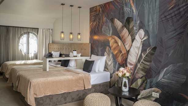 A hotel room with two beds, a large wall mural, a round table with a vase, and a view of the outdoors through a window. - Villa Akacija (Belgrade)