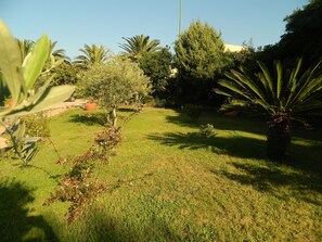 A well-maintained garden with a variety of trees and shrubs, a lawn, and a clear sky. - Le Quattro Lune (Orosei)