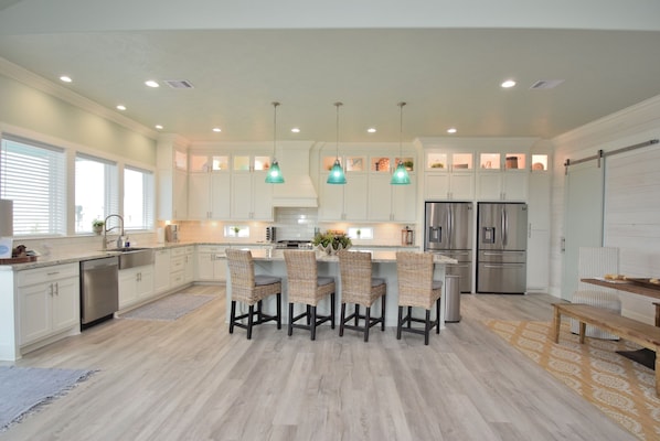 A modern kitchen with white cabinetry, a central island with chairs, stainless steel appliances, and pendant lighting.
