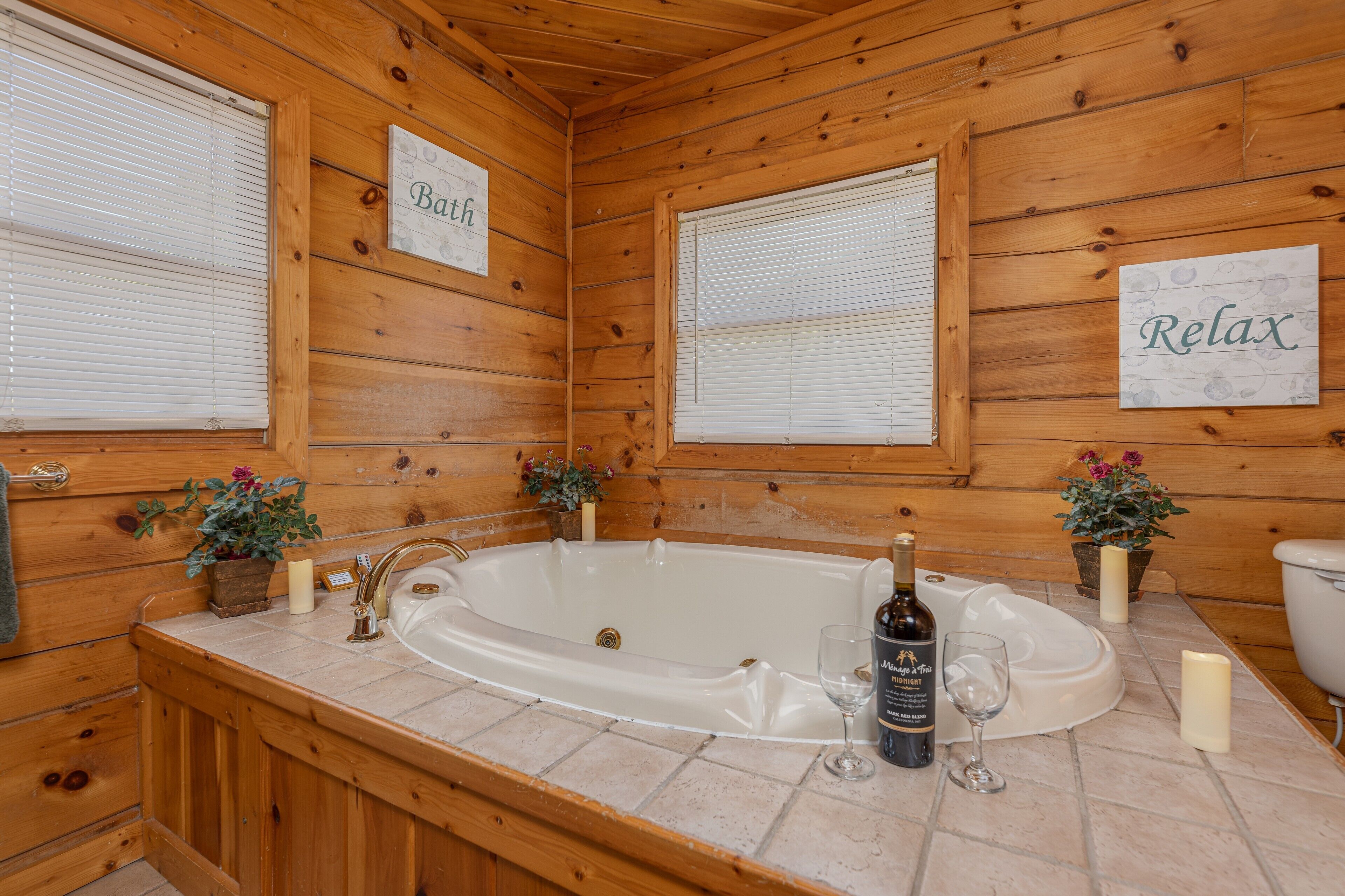 Ein Badezimmer einer Holzhütte mit einer Badewanne, einem Waschbecken und zwei Blumentöpfen.