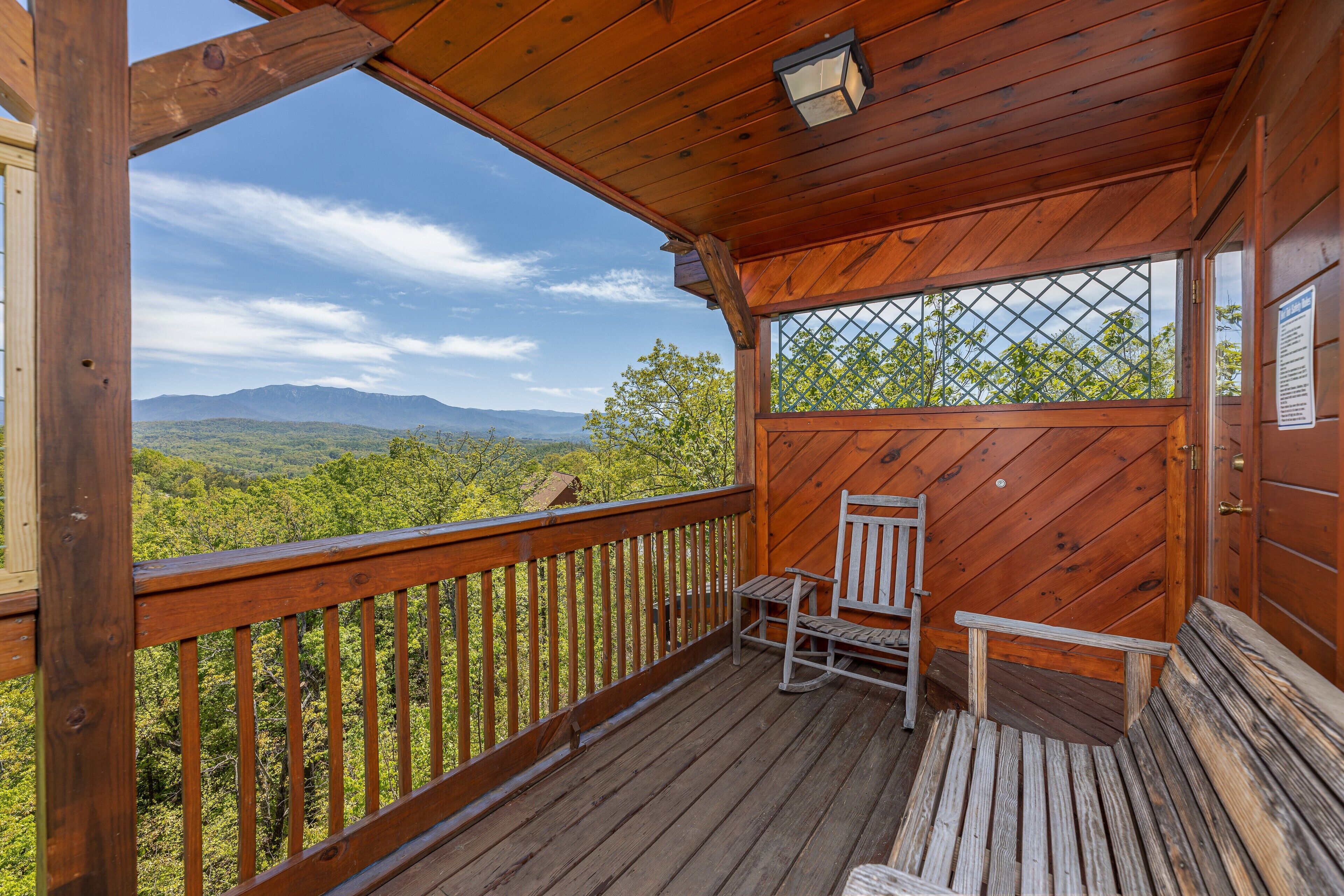 Une terrasse en bois avec un banc et une chaise, d’où l’on peut admirer un paysage boisé avec des montagnes à l’horizon.