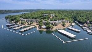An aerial view of a lakeside property with multiple buildings, docked boats, and a swimming area surrounded by dense forest. - Baypoint Village 545 - 3 bdrm condo in Osage Beach (Osage Beach)