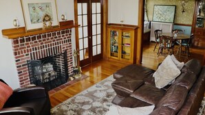A living room with a brick fireplace, a brown leather sofa, a patterned rug, and a dining area with a table and chairs. - The King's Room at TPH - Boston (Boston)