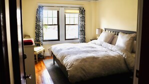 Une chambre à coucher avec un lit, une table de chevet, une chaise et une fenêtre avec des rideaux.