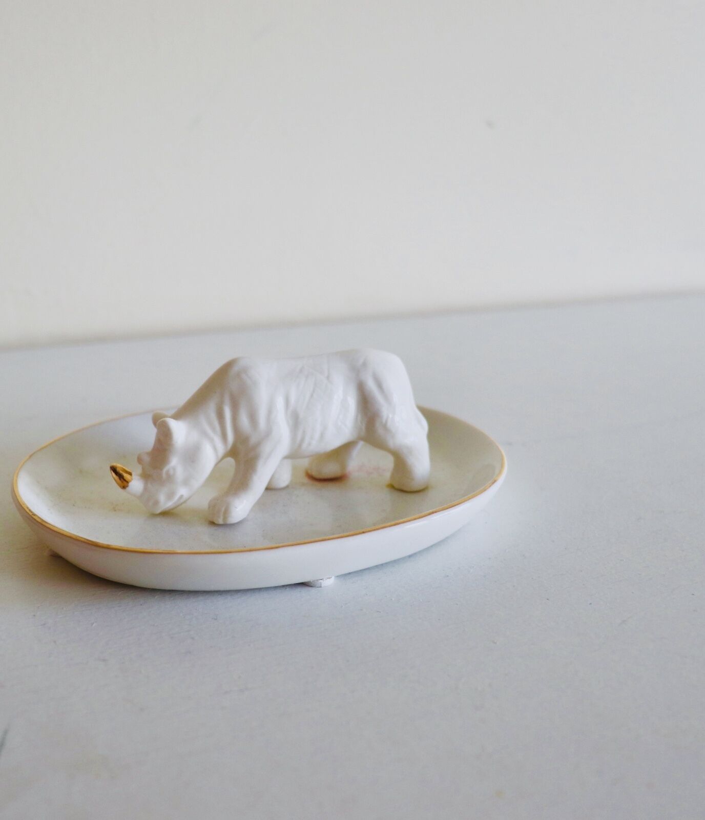 Una escultura de cerámica blanca de un oso sobre un plato blanco con borde dorado.