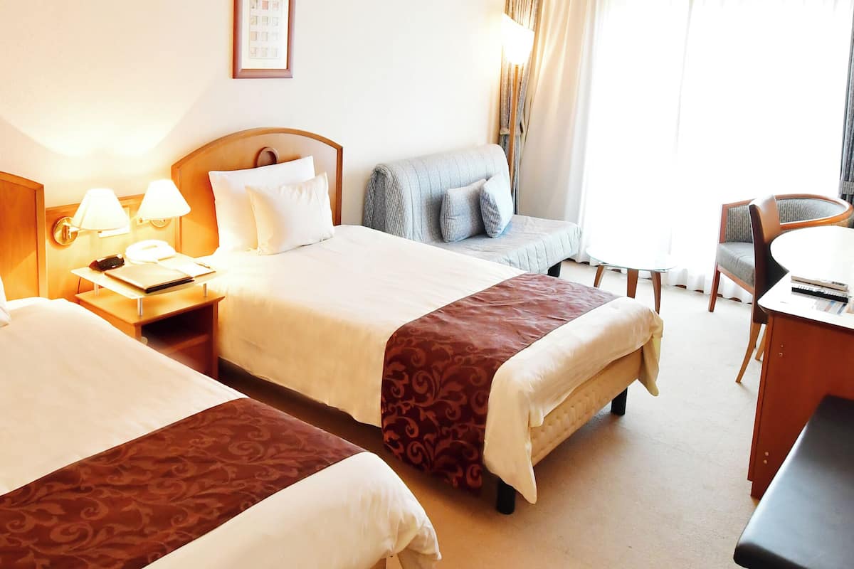 Hotellihuone, jossa on kaksi sänkyä, työpöytä ja tuoli.
