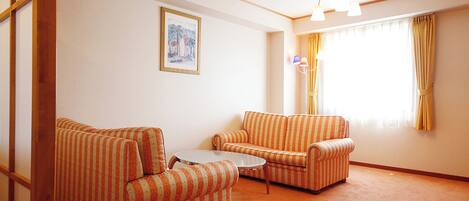 A living room with two striped armchairs, a small round table, and a single window with curtains.