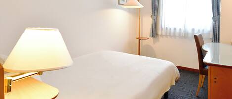 Una habitación de hotel con cama, escritorio, lámpara y silla.