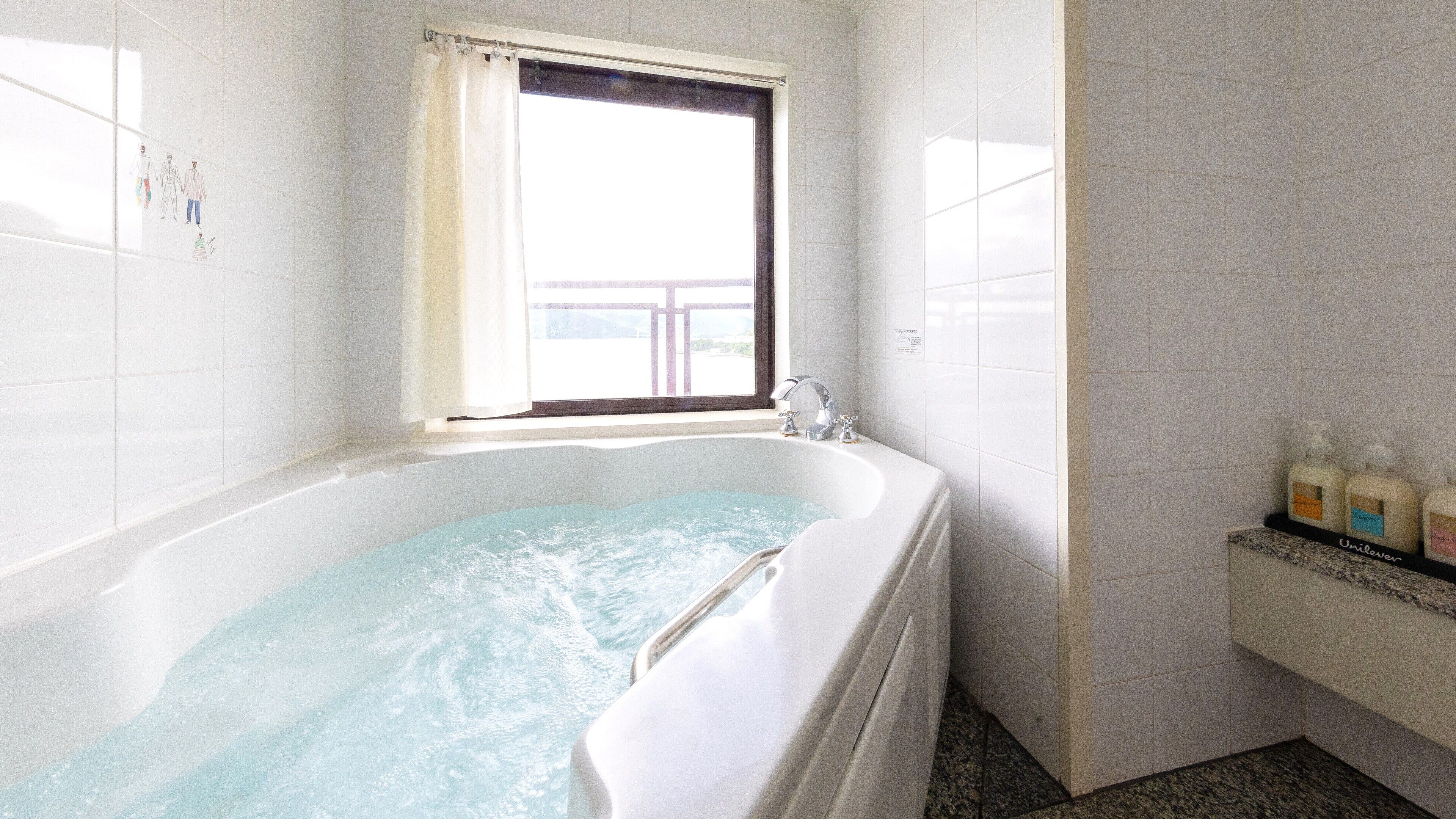 Un baño con bañera, una ventana con cortina y artículos de aseo en un estante.